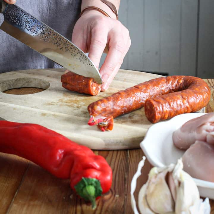 Woman’s hands dicing a whole chorizo on a wooden chopping board