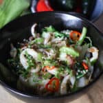 Black bowl filled with stir fried squid, greens, red chilli pepper and chopped coriander