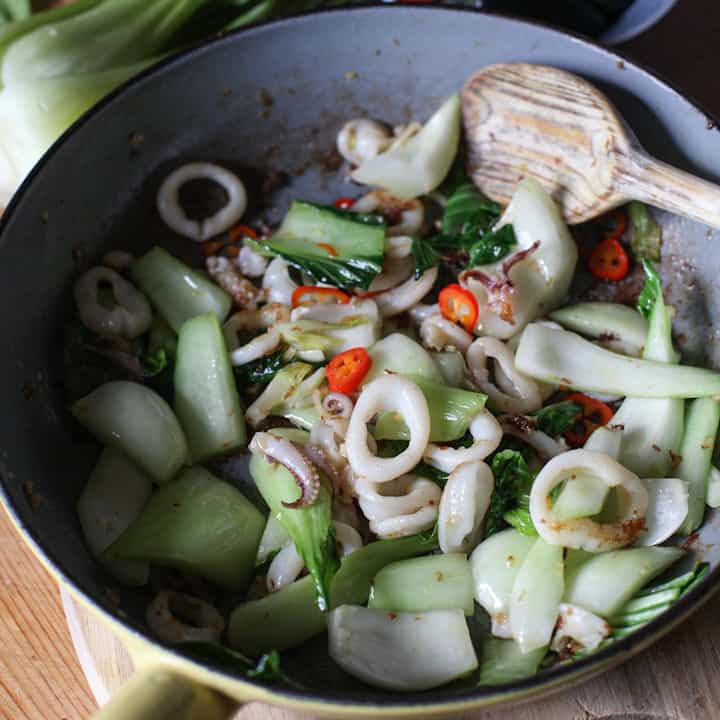 Squid rings, pak Choi, red chilli and lemongrass being stir fried in a grey frying pan