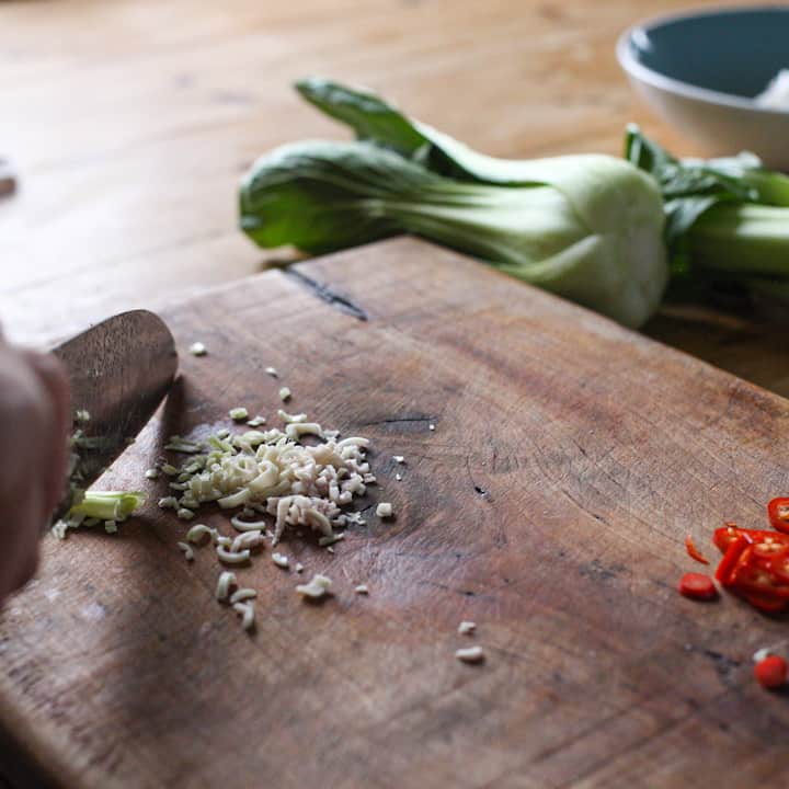 Wooden chopping board with finely chopped lemongrass being prepared with a. Sharp knife