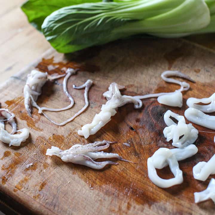 Wooden chopping board with baby squid cut into squid rings and a bright green pak Choi