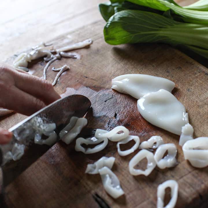 Rings of baby squid being sliced on a wooden chopping board