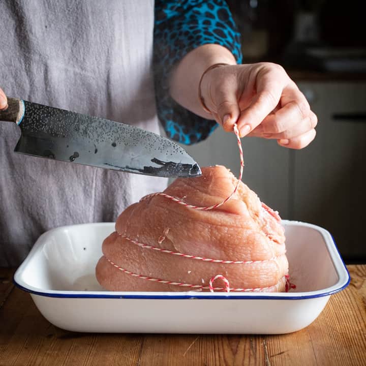 Woman’s hands removing the string from a joint of boiled ham before baking