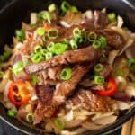 Pan fried steak on a bowl of noodles with chilis and spring onions
