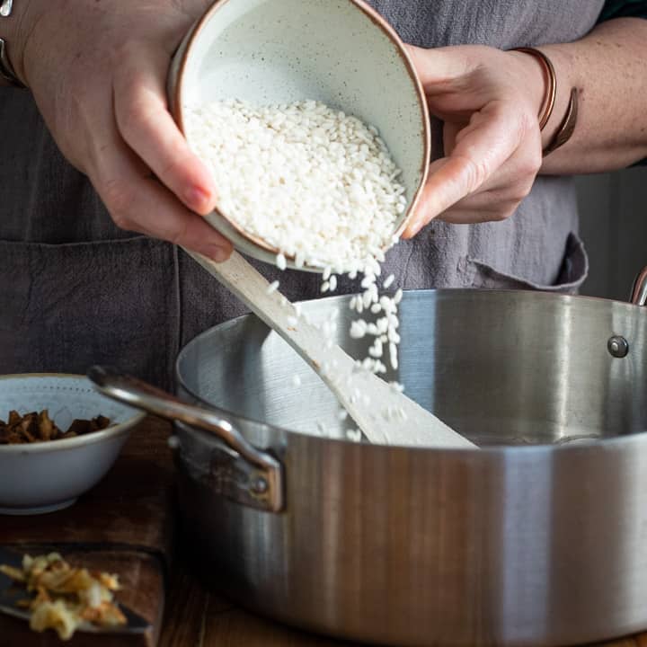 Woman’s pouring arborio rice from a small white bowl into a large silver pan