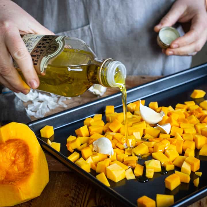 Woman’s hand pouring olive oil from a glass bottle over small pieces of pumpkin