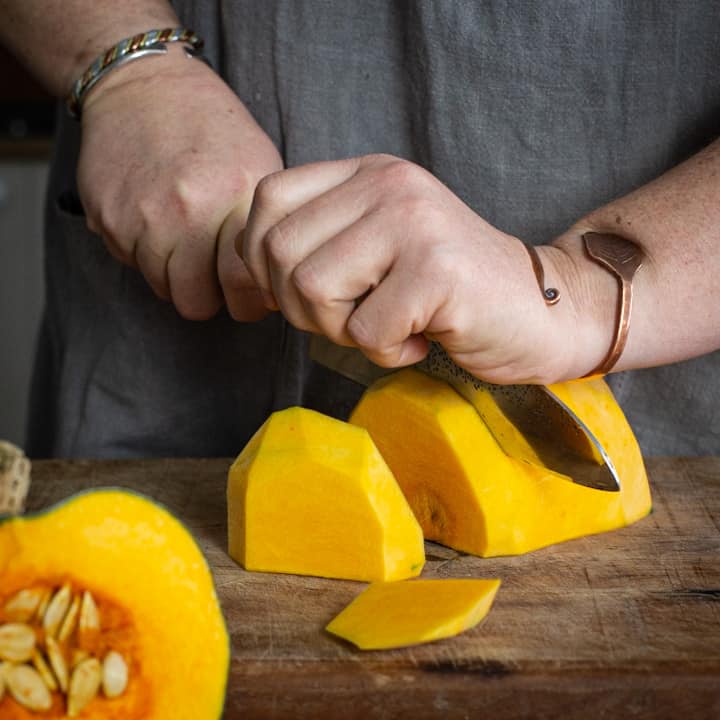 Womans hands cutting an orange pumpkin into a slices on a wooden chopping board