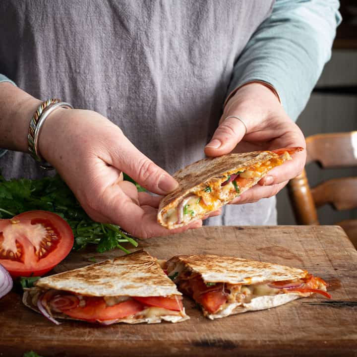 Woman’s holding a quesadilla triangle filled with melted cheese, fresh tomatoes, refried beans and fresh coriander