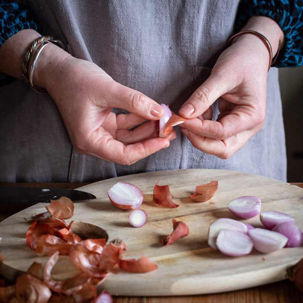 Woman peeling shallots over a wooden kitchen counter
