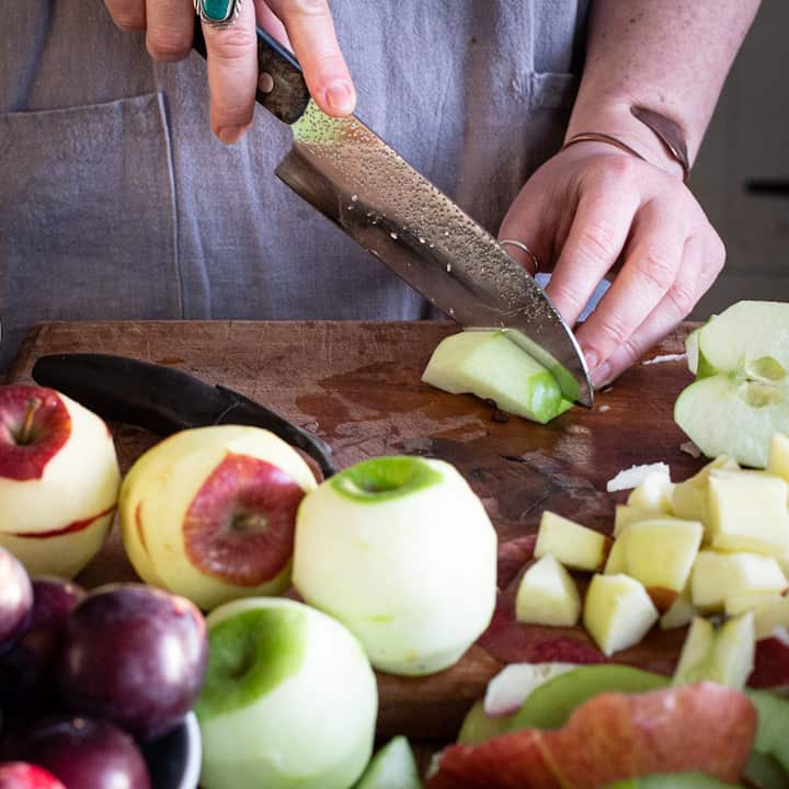 Woman’s hands chopping apples on a dark brown wooden chopping board