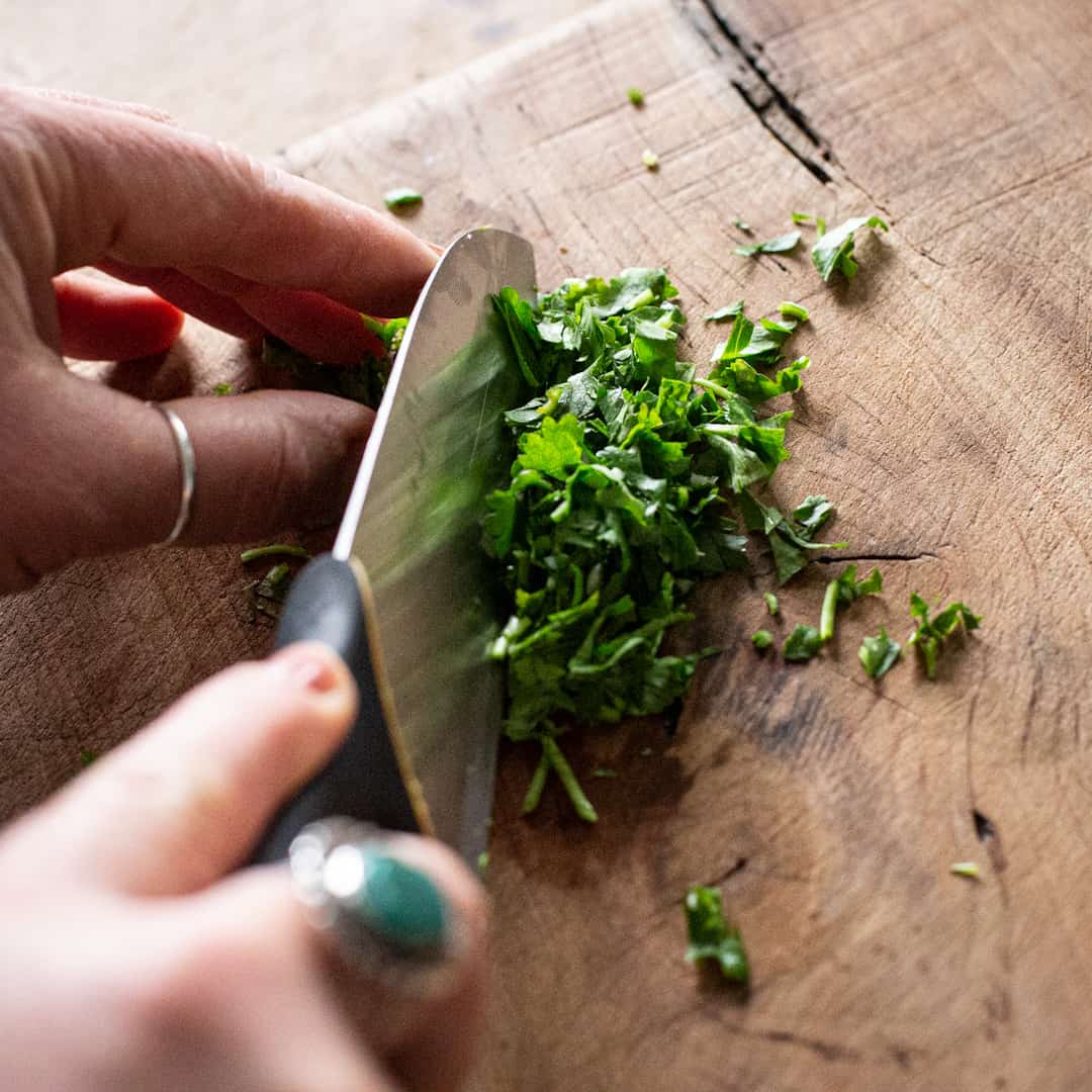 Womans hands chopping fresh parsley on a wooden chopping board