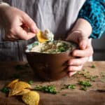 Womans hands scooping butter bean dip from a brown bowl on a wooden kitchen counter