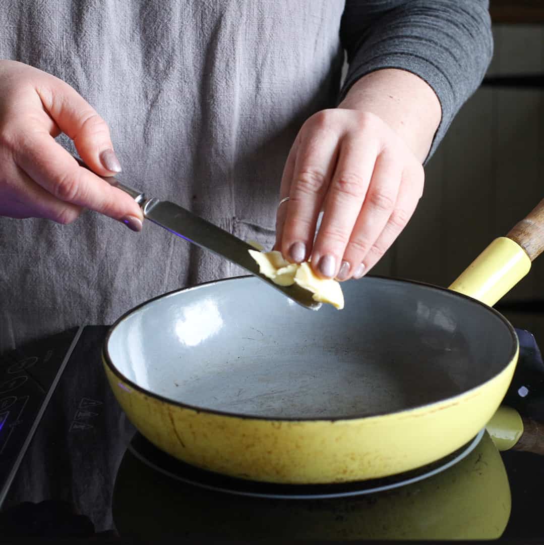 Woman adding butter to a yellow frying pan