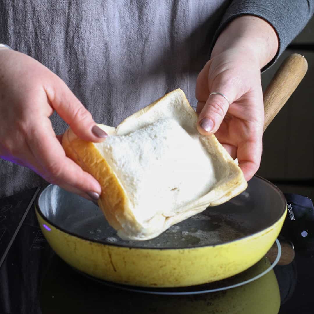Woman holding uncooked toasty over yellow frying pan