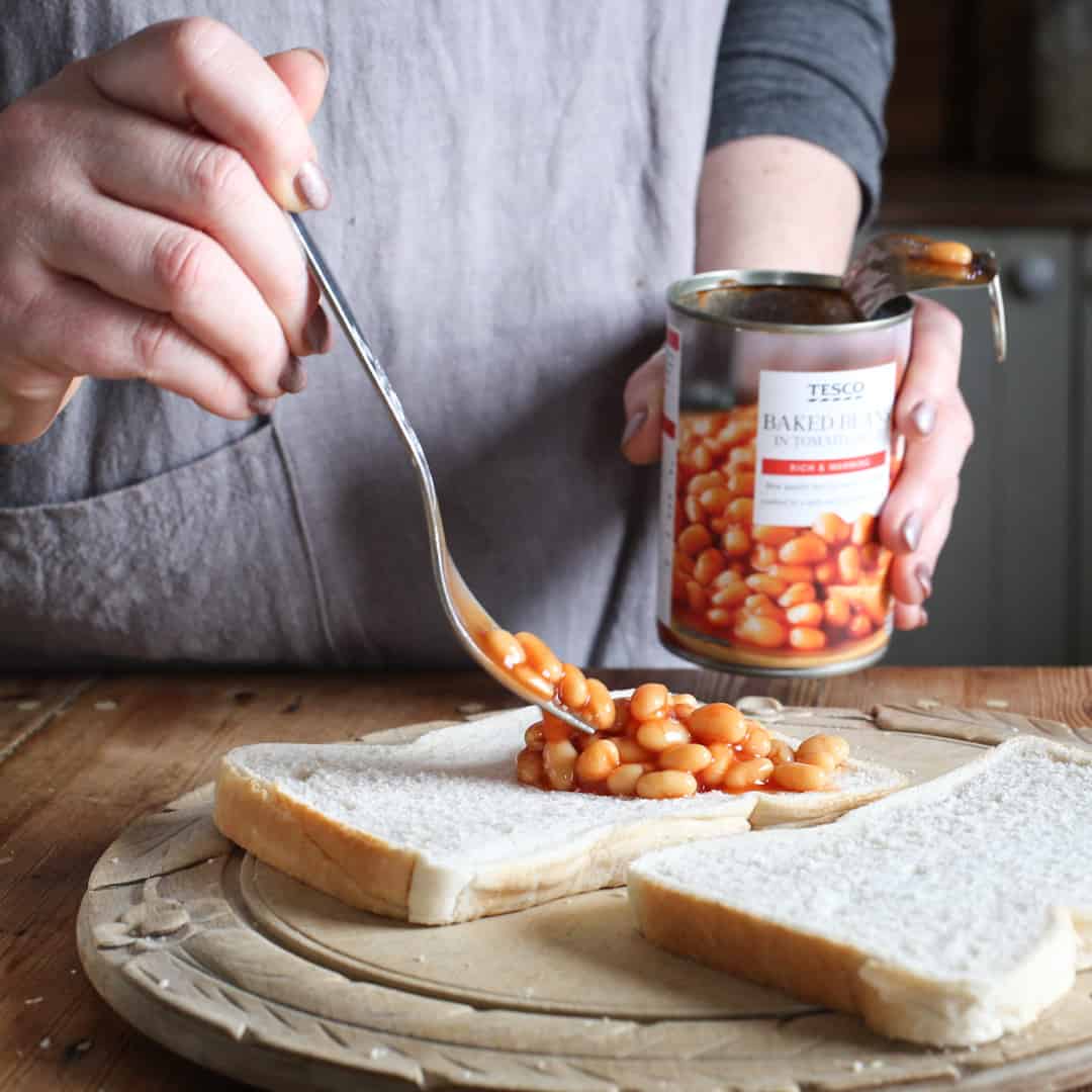 woman spooning baked beans on white bread