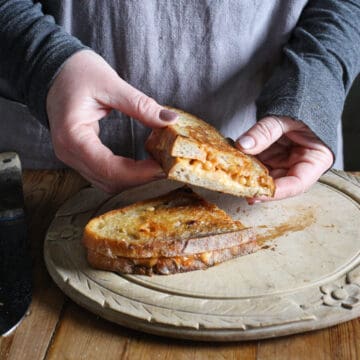 Woman holding cheese and baked bean toasty over wooden platter