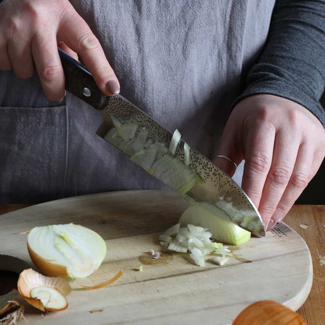 onion being sliced by large knife on wooden board