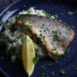 A cooked sea bass fillet on rice and peas in a frying pan