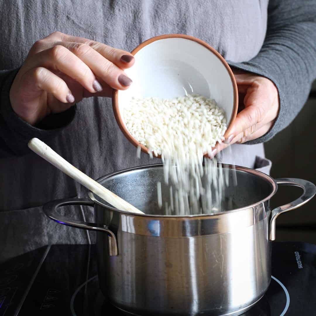 Woman pouring risotto rice into a stainless steel saucepan