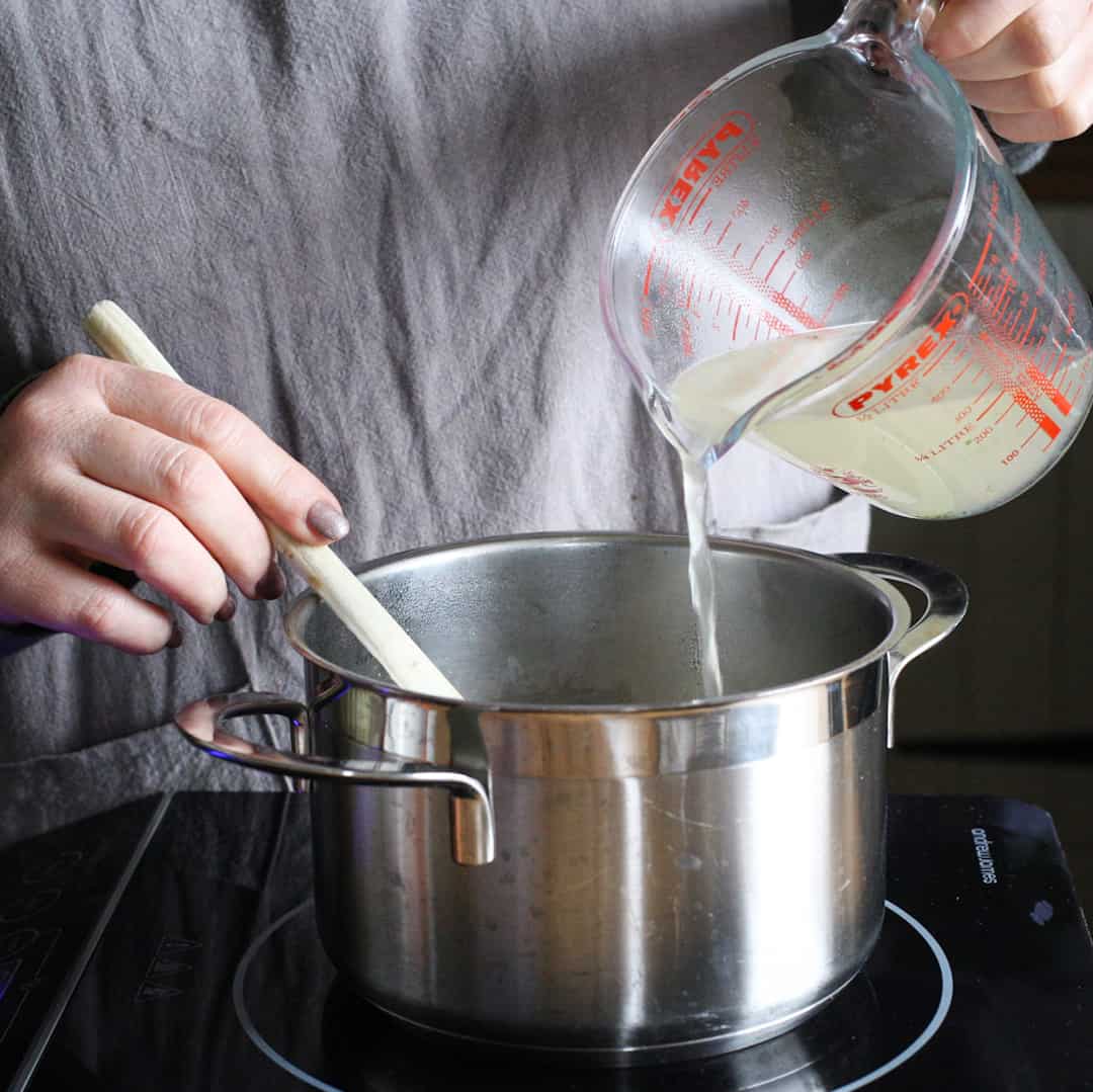 Woman pouring stock into a stainless steel saucepan