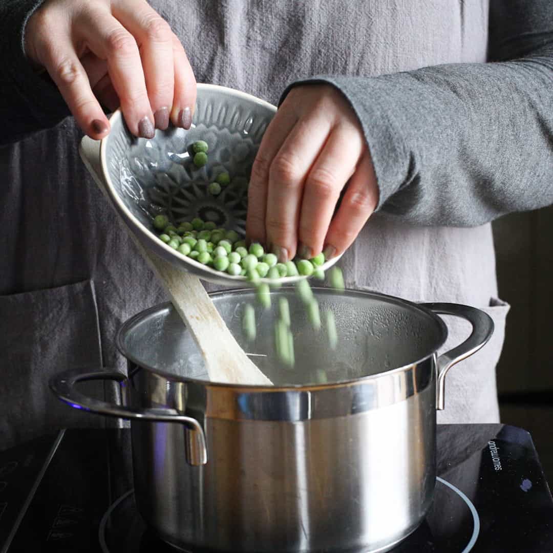 Woman adding frozen peas into stainless steel saucepan