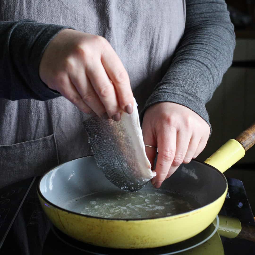 Woman adding a sea bass fillet into a yellow frying pan