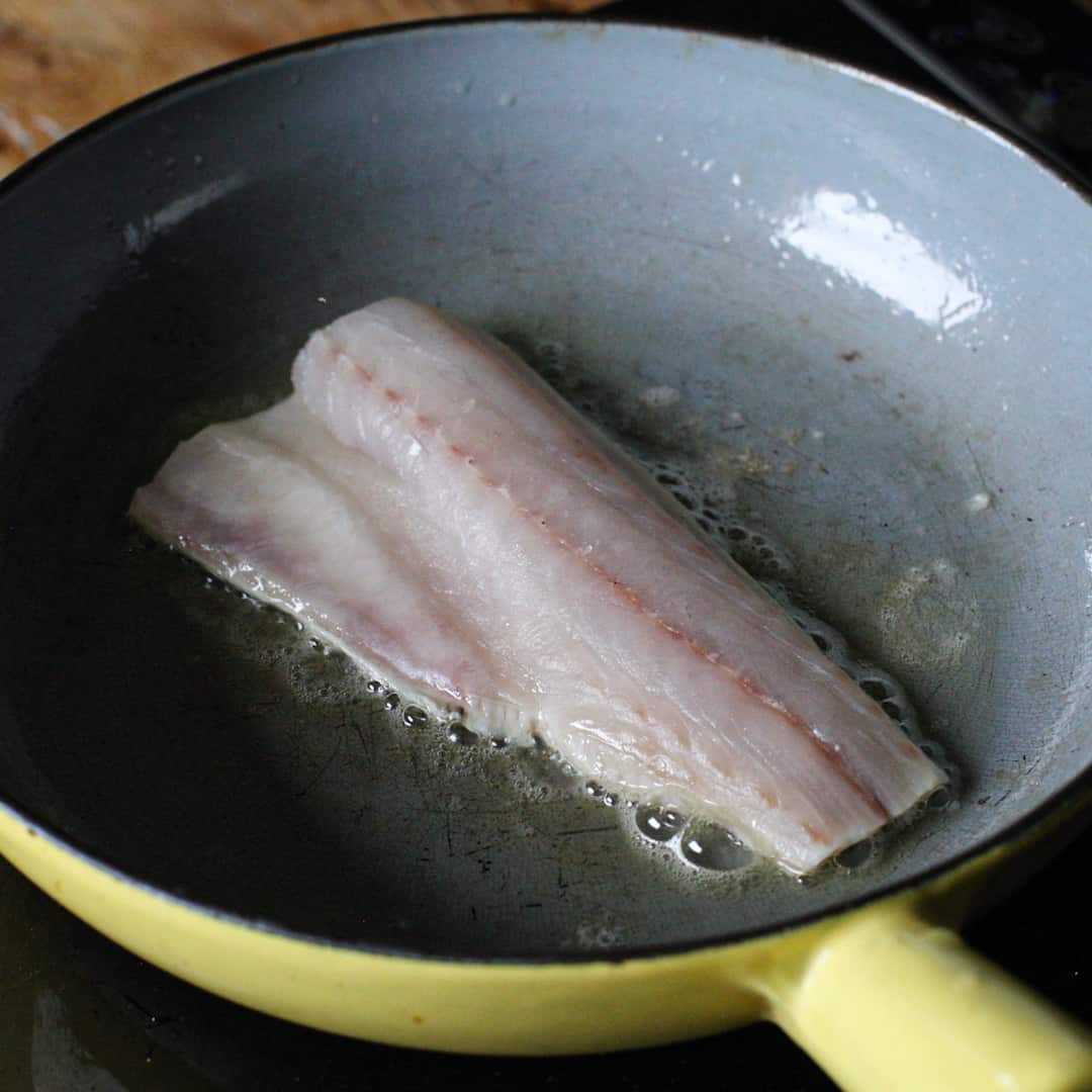 A sea bass fillet in a frying pan