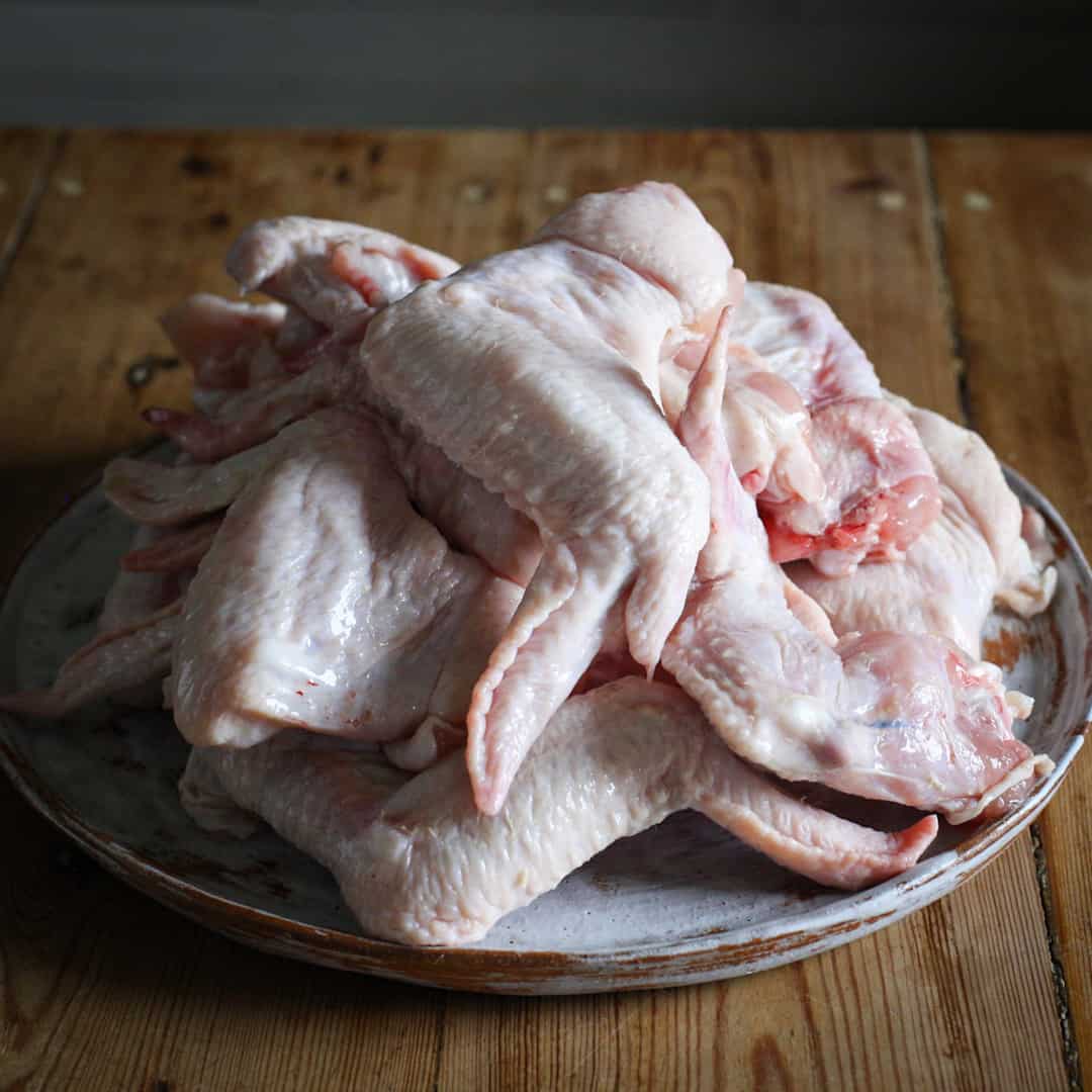 Whit pate on wooden kitchen counter piled high with several raw chicken wings