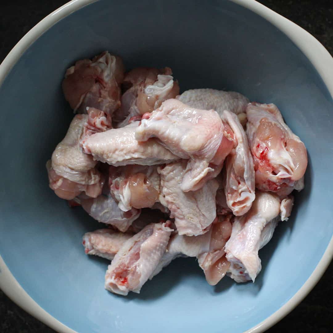 Inside shot of a pale blue mixing bowl half filled with chicken wings ready to marinade and cook