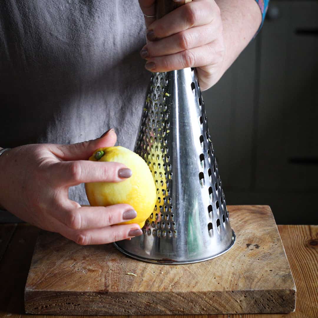 Womans hands grating a lemon on a tall silver cheese grate