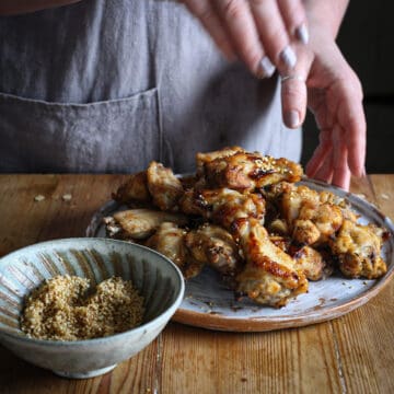 Woman sprinkling toasted sesame seeds over a white plate of honey lemon pepper chicken wings