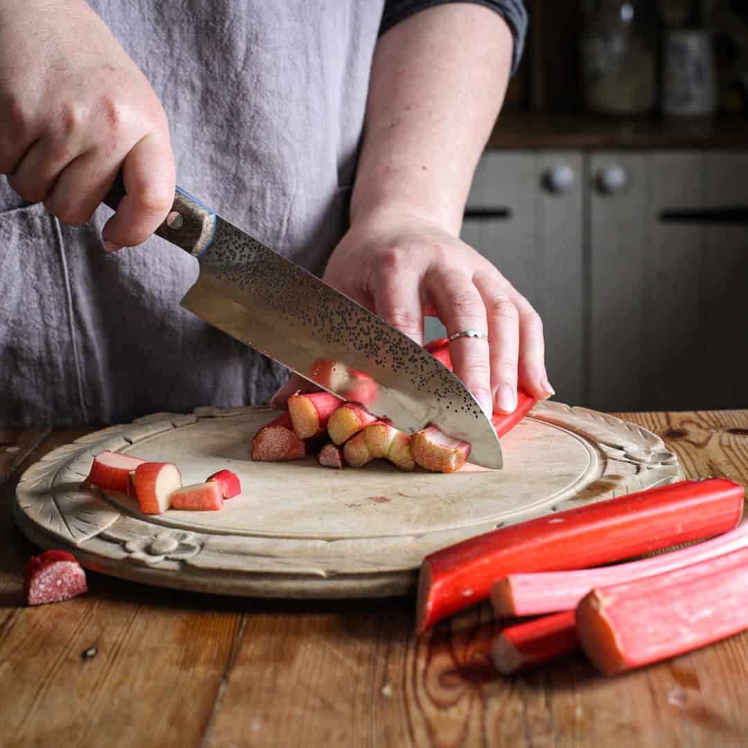Woman in grey slicing fresh rhubarb stalks on a wooden chopping board