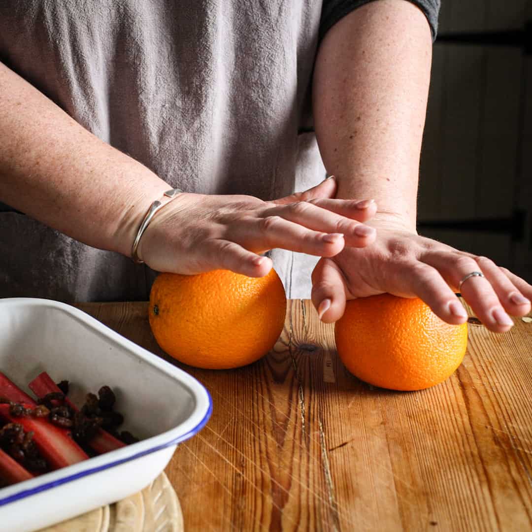 Woman rolling 2 large oranges on a wooden kitchen counter before squeezing for juice