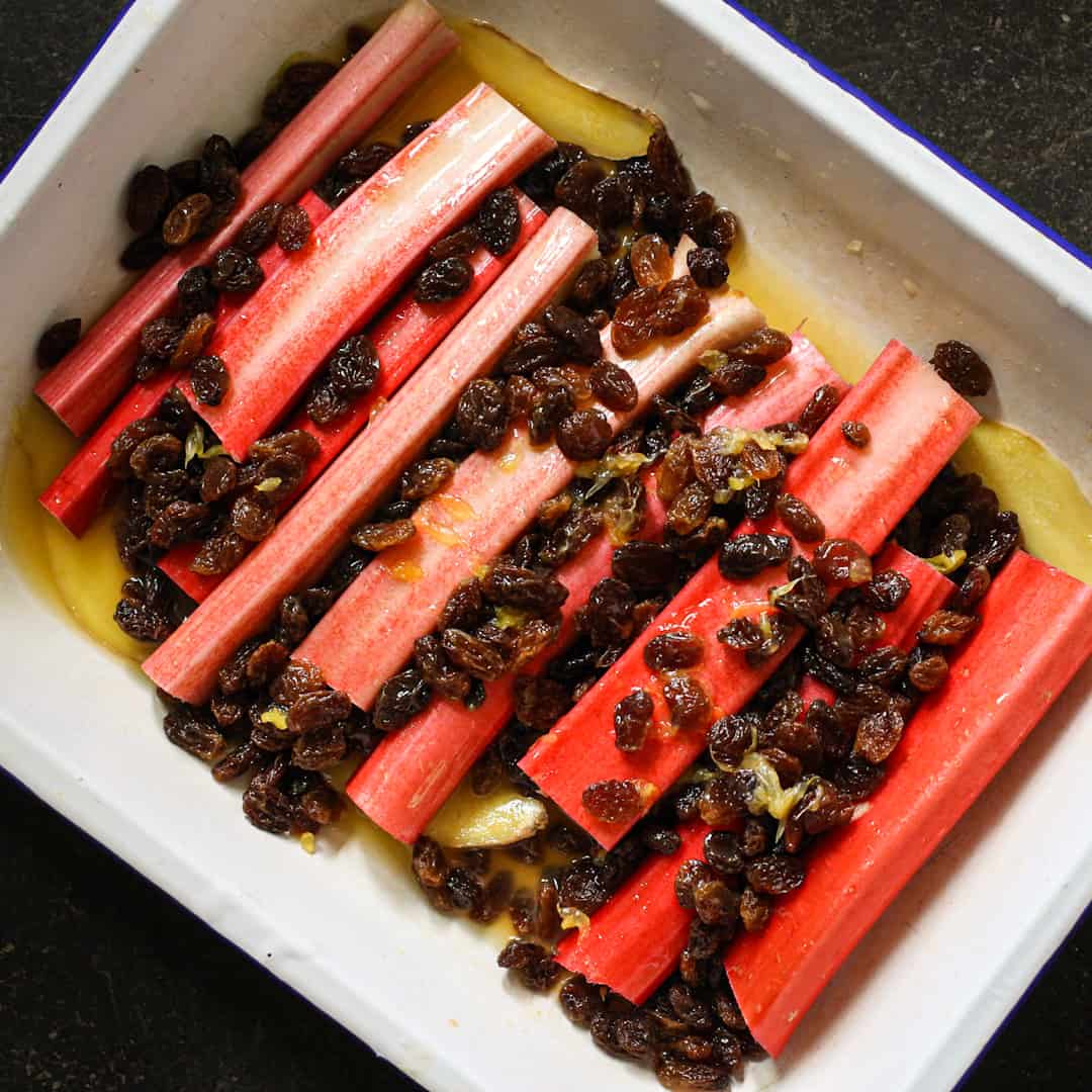 White enamel baking dish filled with fresh stalks of rhubarb, sultanas and orange juice for baking