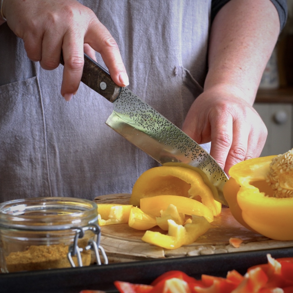 Womans hands slicing a yellow bell pepper on a wooden chopping board