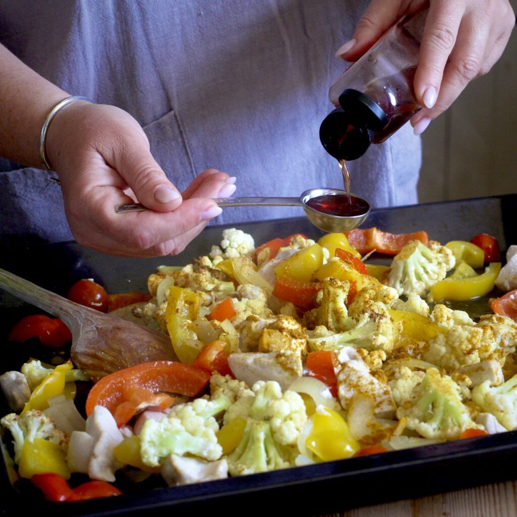 Woman measuring out red wine vinegar onto a sheet pan of chopped chicken and veggies