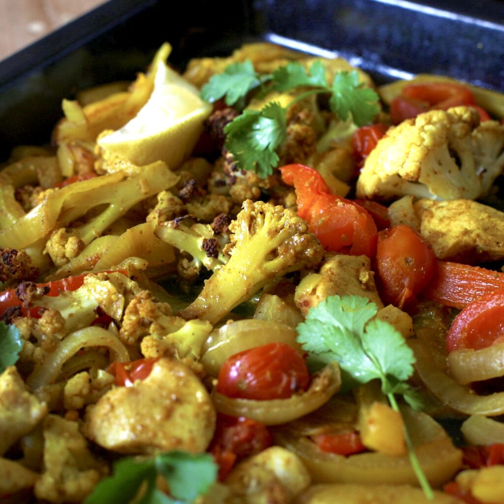 Black baking tray filled with curry roast vegetables and pieces of chicken topped with green coriander leaves