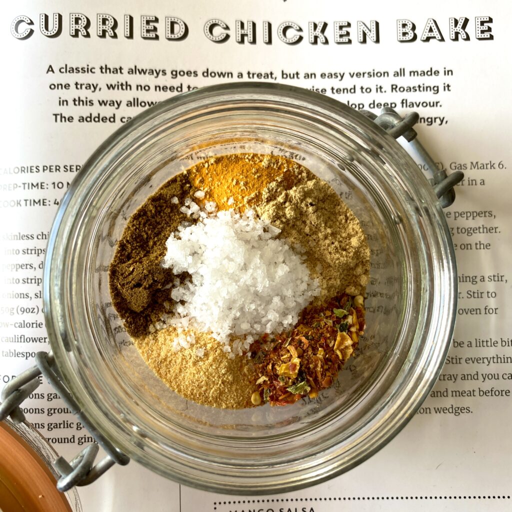 Small glass jar of mixed curry spices on the page of a cookbook showing the recipe