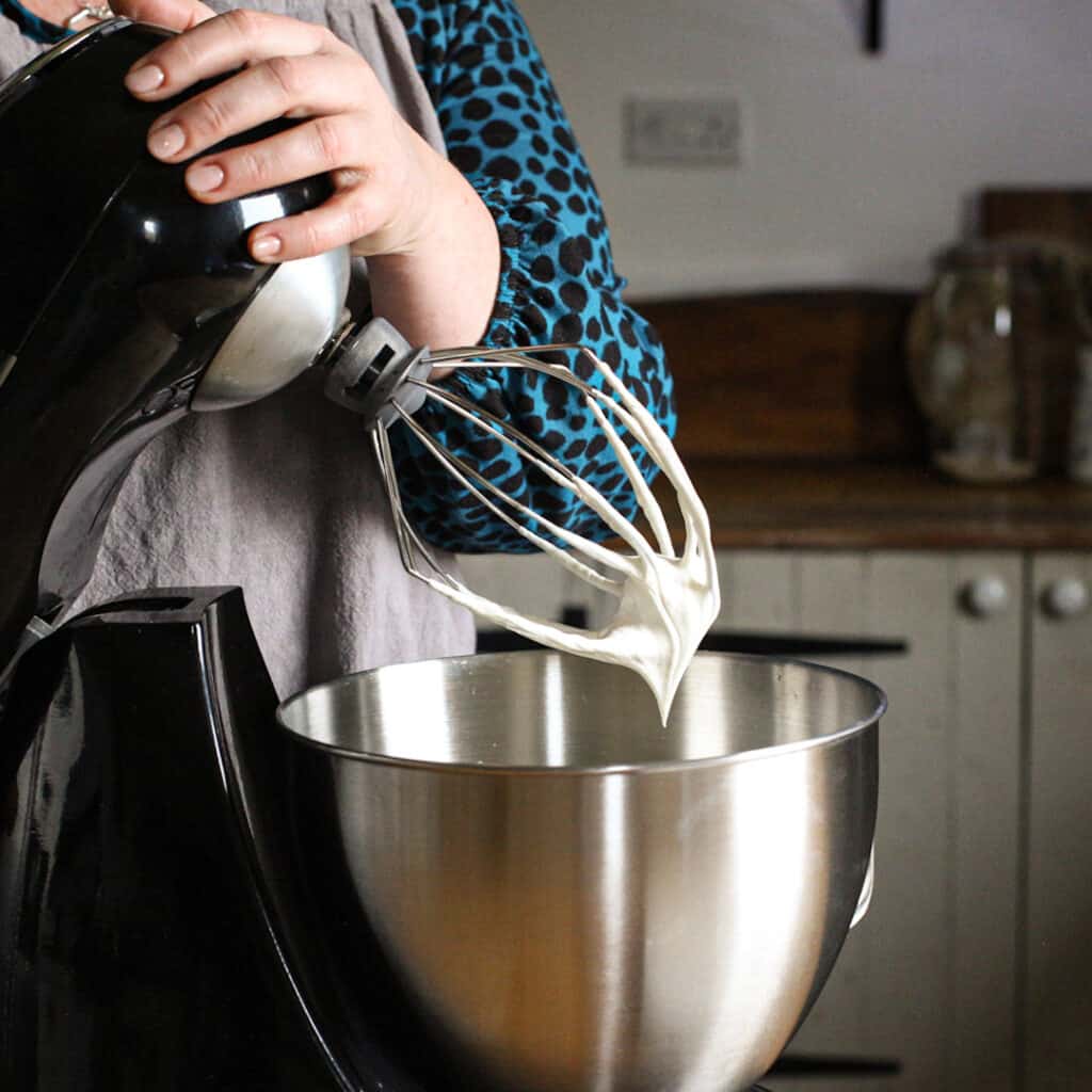 Womans hands lifting the whisk attachment from a black electric stand mixer after whipping cream