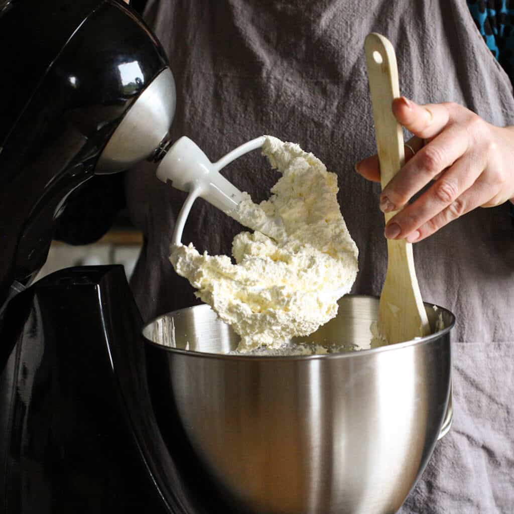 Womans hands scraping down the sides of a silver mixer bowl of cream