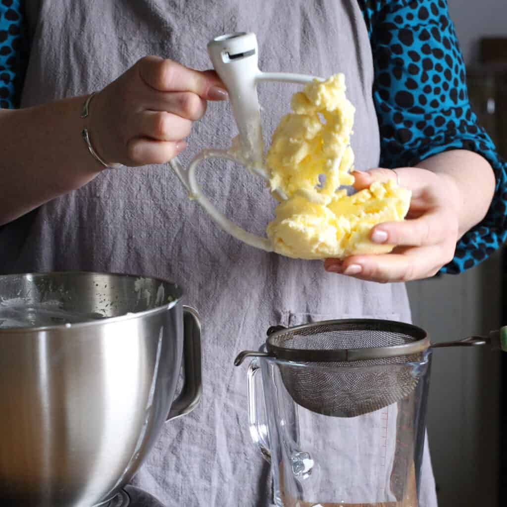 Woman in grey removing fresh butter from a mixer dough hook before squeezing out the buttermilk