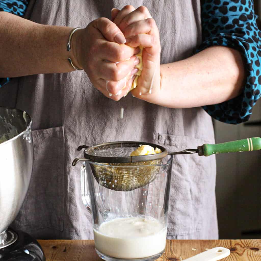 Woman in grey pressing a lump of homemade butter in her hands to extract the buttermilk before storing