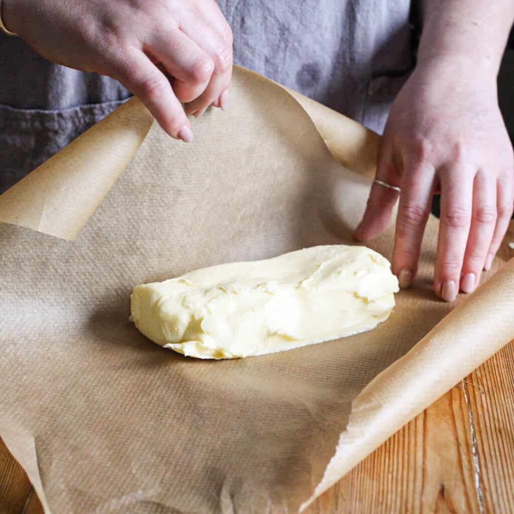Woman rolling fresh homemade butter up into a sausage shape with a piece of brawn baking paper