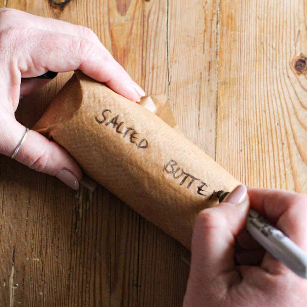 Womans hands writing ‘salted butter’ onto a brown baking paper roll filled with freshly made butter