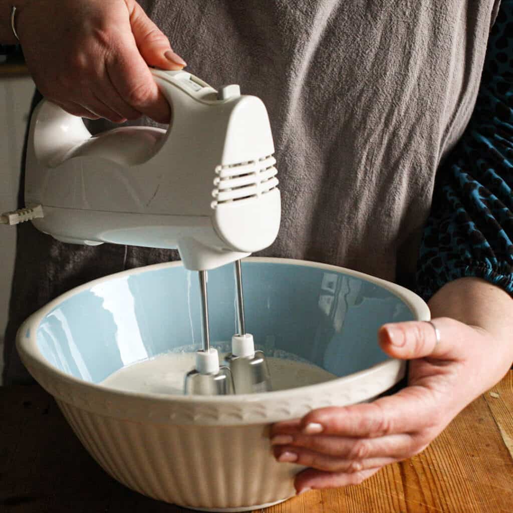 Woman whipping double cream with an electric whisk in a large blue and white mixing bowl
