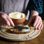 Woman in grey spreading fresh homemade butter onto a pieces of sourdough toast on a wooden chopping board