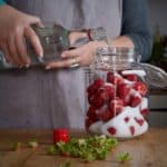 Woman topping up a glass jar of strawberries and sugar with vodka