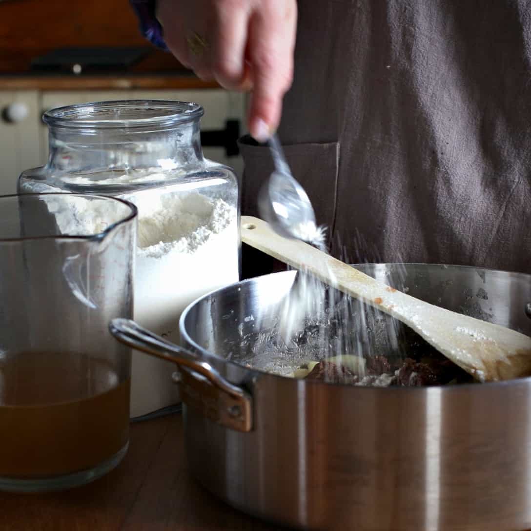 Woman sprinkling flour from a silver spoon into a large silver pan
