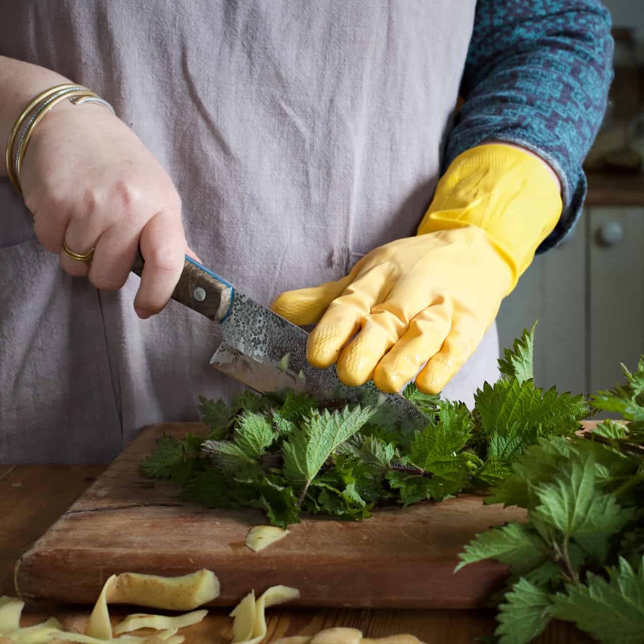Woman wearing bright yellow rubber gloves chopping stinging nettles on a wooden chopping board