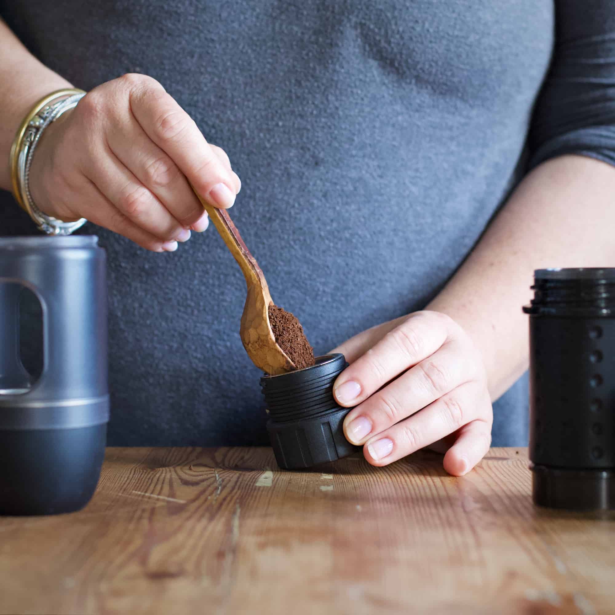 Womans hands scooping freshly ground coffee beans into an espresso maker